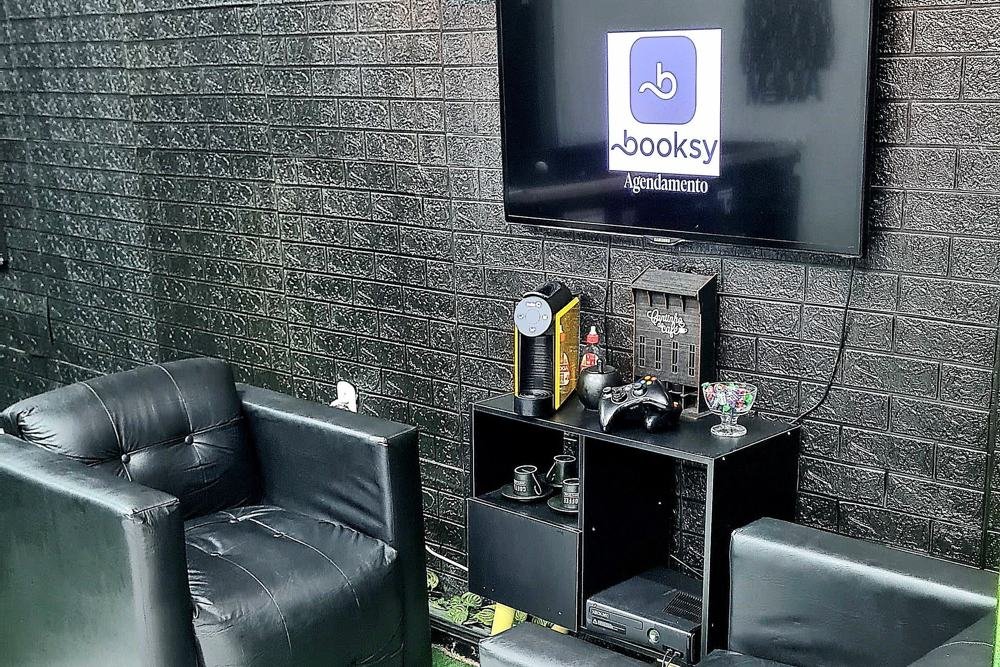 Lounge de espera com poltronas de couro e TV com a agenda do dia